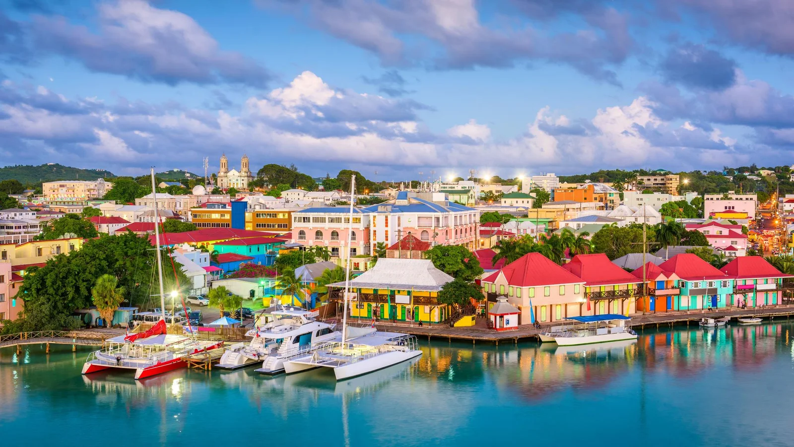 Puerto colorido de Antigua al atardecer con casas pastel, techos rojos y catamaranes