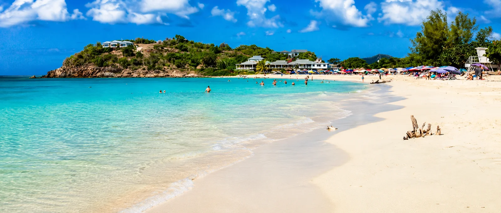 Playa de arena blanca con aguas turquesa, sombrillas de colores y bañistas